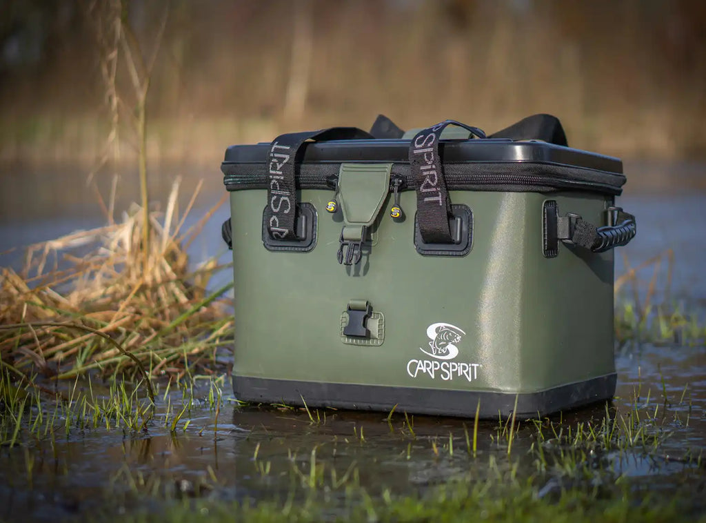An olive green, rectangular, waterproof fishing cooler or tackle box with a black lid and carry straps.
